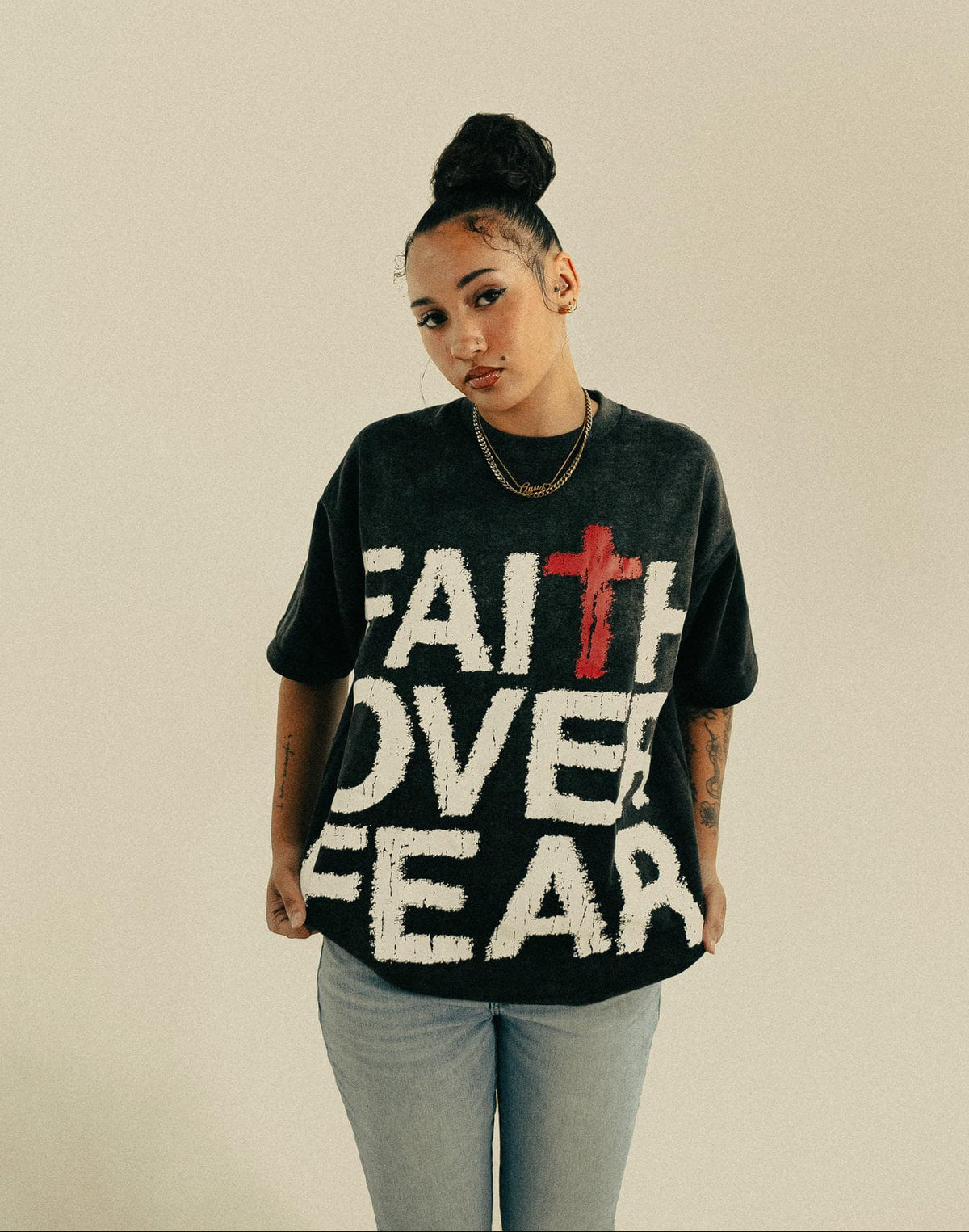 Person wearing a black t-shirt with 'Faith Over Fear' text and a red cross on a beige background