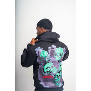 A man wearing black hoodie with a design that shows pictures of green skulls and a R3Birth logo on the back